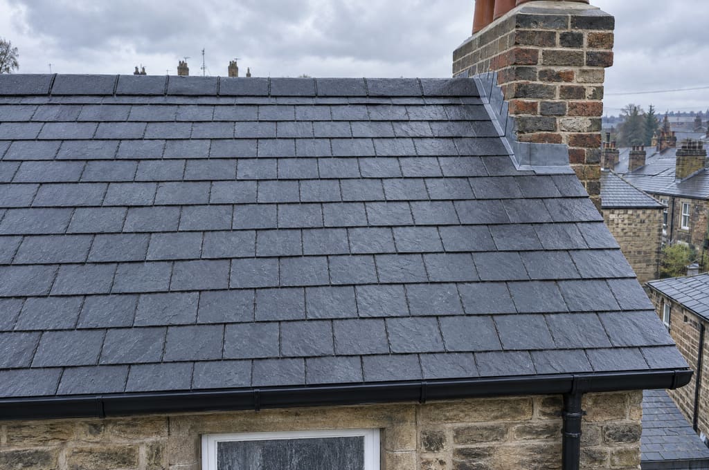 After: the same roof with every slate back in straight courses, new lead flashing on the chimney and a new black gutter